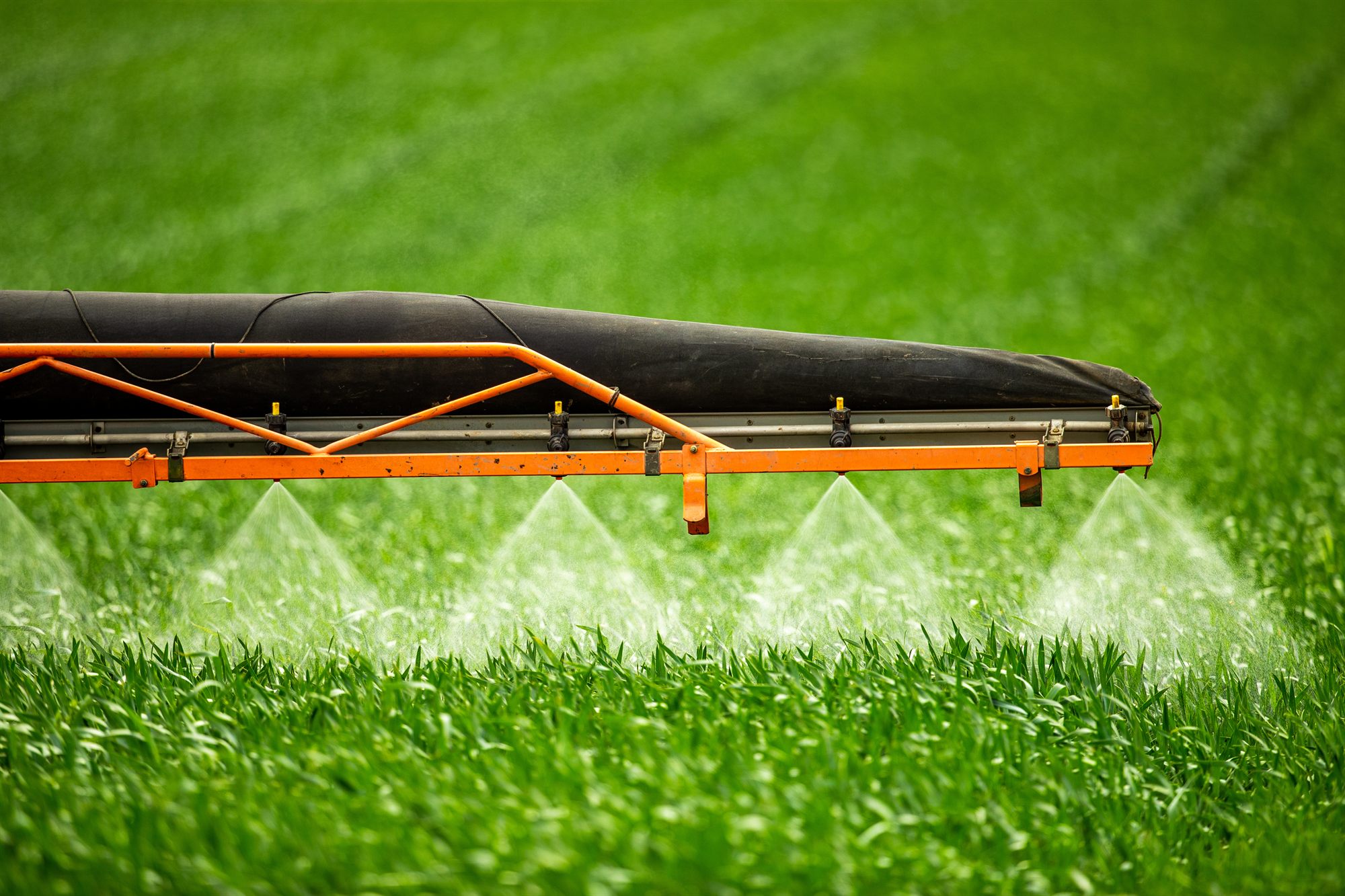 Boom sprayer applying biocidal product across a green field